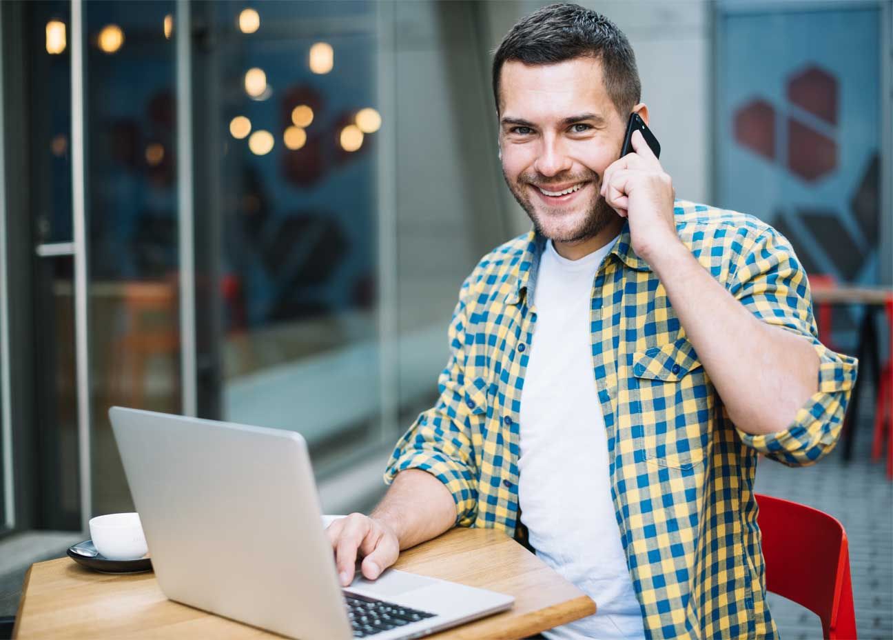 autónomo sonriendo con el portátil y un teléfono